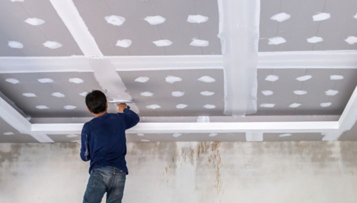 Un albañil instalando placas de yeso laminado. 